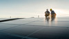 Zwei Arbeiter stehen hinter einer Photovoltaikanlage und besprechen sich.